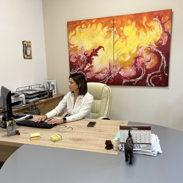 Kancelarija sa stolom bez boje i polukruznim delom sive boje. Na stolu je kompjuter i direktor firme na svom radnom mestu. Zidovi su bele boje a na zidu je slika nepoznatog autora na kojoj preovladavaju crvena i zuta boja.